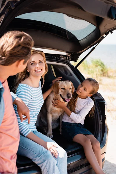 Foco seletivo da mulher olhando para o marido perto da filha e golden retriever no porta-malas do carro — Fotografia de Stock