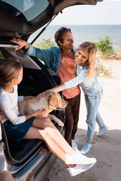 Enfoque selectivo de la familia con golden retriever de pie cerca de coche en la playa - foto de stock