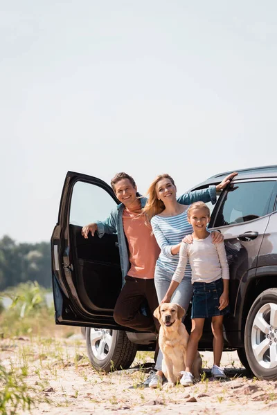 Foco seletivo da família com golden retriever olhando para a câmera enquanto está perto do carro ao ar livre — Fotografia de Stock
