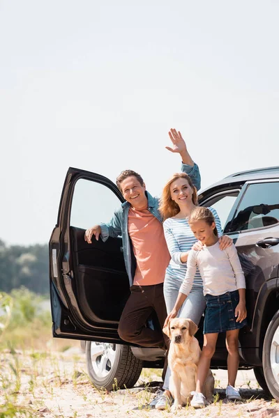 Focus selettivo dell'uomo agitando mano vicino alla famiglia con golden retriever e auto all'aperto — Foto stock