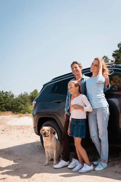 Familia con golden retriever de pie junto al coche al aire libre - foto de stock