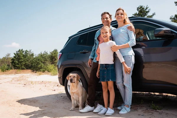 Малюк стоїть біля батьків і золотий ретривер під час подорожі на машині — стокове фото
