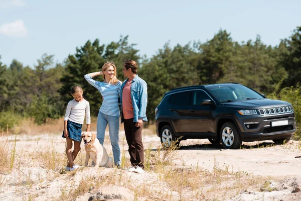 Selective focus of family with golden retriever standing near car during weekend — Stock Photo