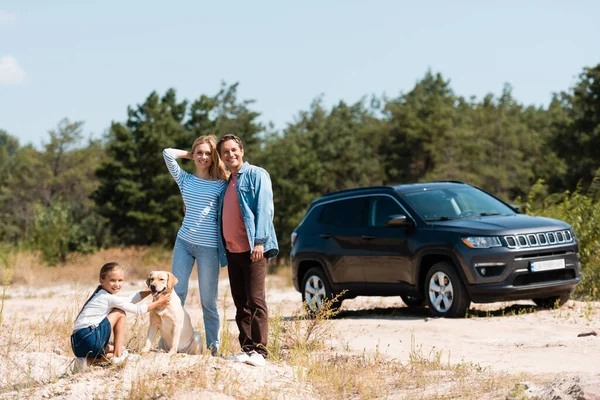 Selective focus of man hugging wife near daughter with golden retriever during vacation — Stock Photo