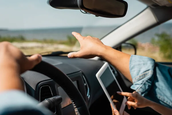 Ausgeschnittene Ansicht eines Mannes, der mit dem Finger in die Nähe seiner Frau zeigt, mit digitalem Tablet im Auto — Stockfoto