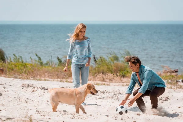 Coppia con calcio e golden retriever che gioca in spiaggia durante il weekend — Foto stock