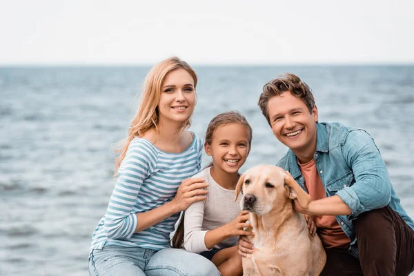 Família com golden retriever olhando para a câmera na praia — Fotografia de Stock