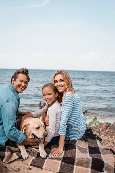Family with golden retriever looking at camera while sitting on blanket — Stock Photo