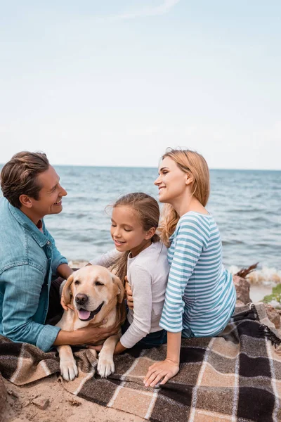 Pais olhando uns para os outros perto golden retriever e criança à beira-mar — Fotografia de Stock