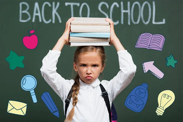 Foyer sélectif de l'écolière mécontente tenant des livres au-dessus de la tête près du tableau noir avec retour à l'école lettrage et illustration — Photo de stock