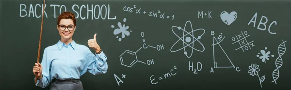 Panoramic shot of chemistry teacher with pointing stick showing thumb up near chalkboard with back to school lettering and illustration — Stock Photo