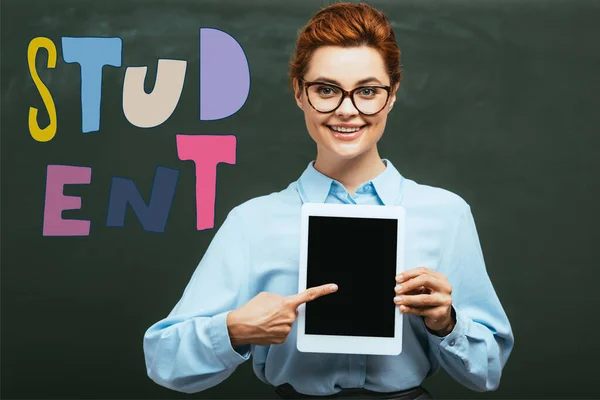 Profesor señalando con el dedo a la tableta digital con pantalla en blanco cerca de pizarra con letras de estudiante - foto de stock