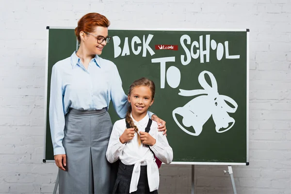 Enseignant et écolière debout près de tableau noir avec lettrage de retour à l'école — Photo de stock