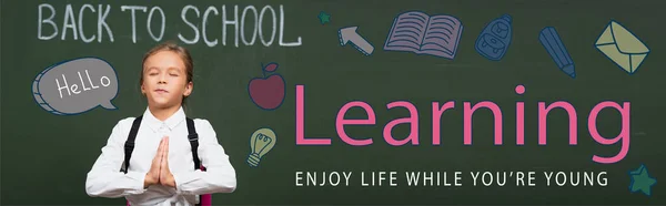 Panoramic concept of schoolgirl with praying hands near chalkboard with back to school, learning enjoy life while you are young lettering — Stock Photo
