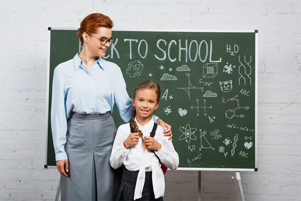 Lehrerin und Schülerin stehen neben Kreidetafel mit Schulbuchstaben — Stockfoto