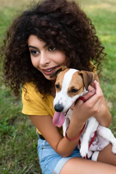 Selective focus of young woman holding dog and looking away — Stock Photo