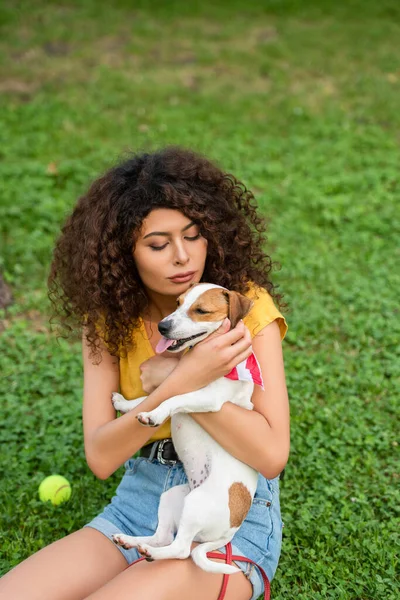 Selective focus of young woman sitting and holding dog on grass — Stock Photo
