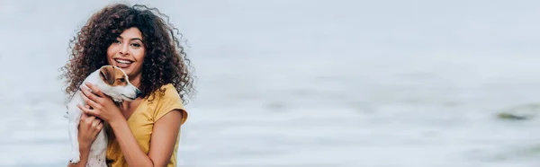 Горизонтальное изображение веселой женщины, обнимающей Джека Рассела терьера возле реки — стоковое фото