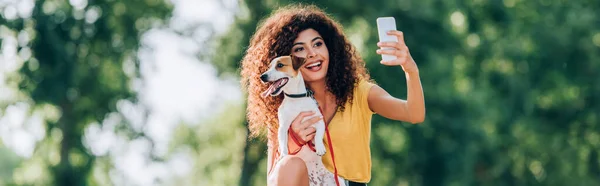 Concepto horizontal de mujer emocionada tomando selfie en el teléfono móvil con jack russell terrier perro - foto de stock