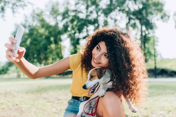 Joyful woman taking selfie on smartphone with jack russell terrier dog in park — Stock Photo