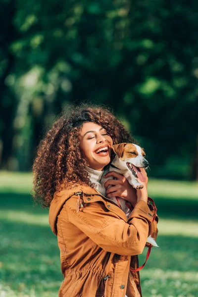 Mujer joven en impermeable abrazando jack russell terrier en el parque - foto de stock