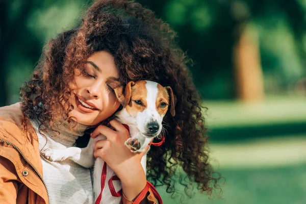 Junge Frau mit geschlossenen Augen umarmt Jack Russell Terrier im Freien — Stockfoto