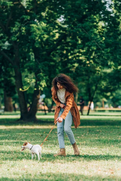 Selektiver Fokus einer Frau im Regenmantel, die an der Leine auf einer Wiese im Park läuft — Stockfoto