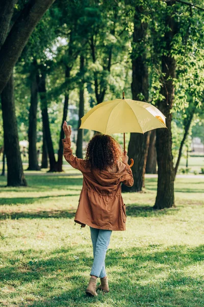 Вид на молодую женщину в осеннем наряде, держащую зонтик во время прогулки в парке — стоковое фото