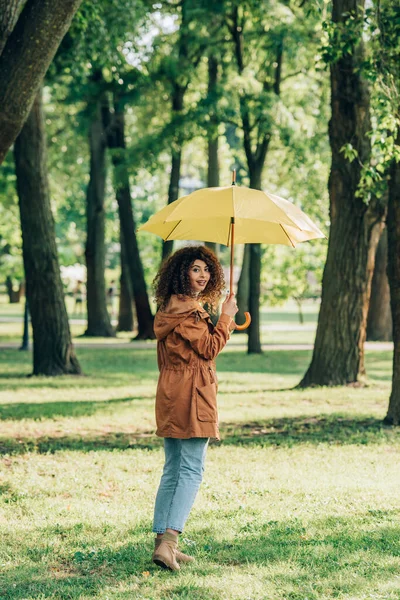 Селективный фокус женщины с зонтиком, смотрящей на камеру на лугу в парке — стоковое фото