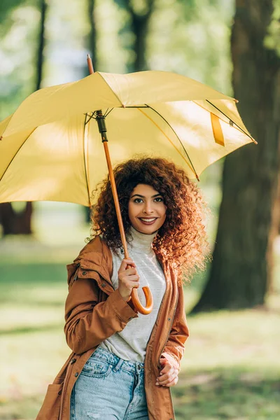 Mujer joven en traje de otoño sosteniendo paraguas y mirando a la cámara en el parque - foto de stock