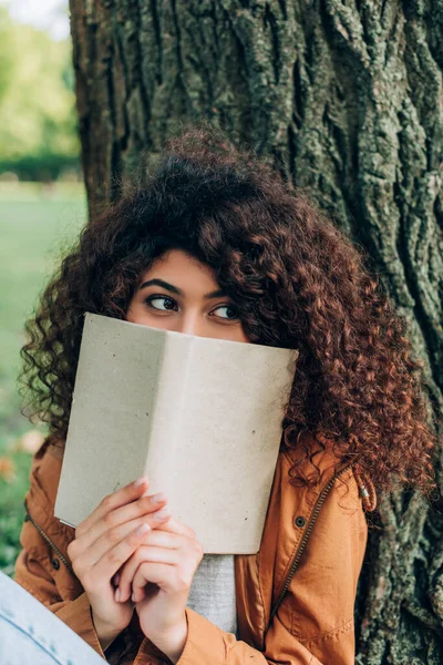 Selective focus of woman holding book near tree in park — Stock Photo