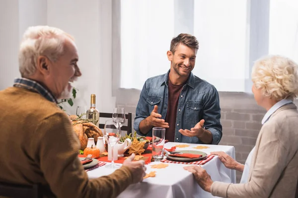 Hombre excitado haciendo gestos mientras habla con los padres mayores durante la cena de acción de gracias - foto de stock