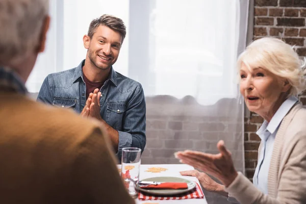 Freudiger Mann mit Gebetsgeste und Seniorin, die mit der Hand zeigt, während sie Erntedank feiert — Stockfoto