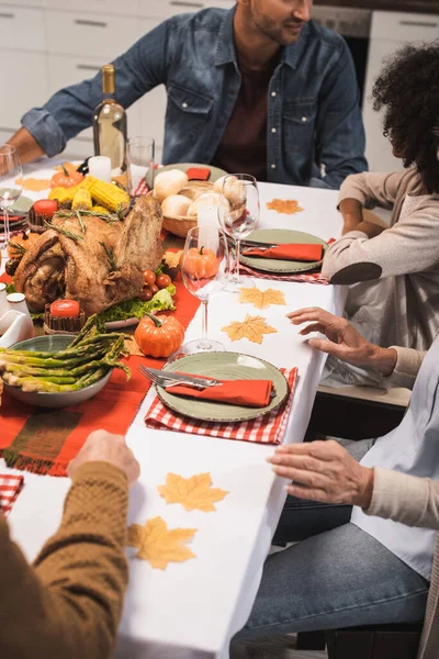 Vista recortada de la familia multicultural sentada en la mesa servida con cena de acción de gracias - foto de stock