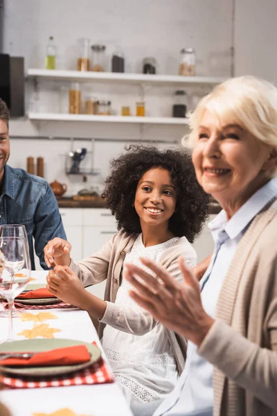 Selektiver Fokus der fröhlichen Seniorin gestikuliert beim Dankessen mit multikultureller Familie — Stockfoto