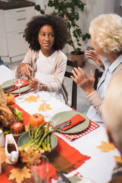 Senior woman gesturing while talking to african american girl during celebration of thanksgiving — Stock Photo