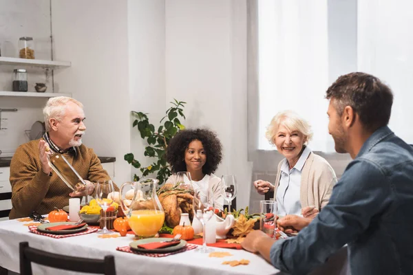 Senior man holding bottle of white wine during thanksgiving dinner with multicultural family — Foto stock