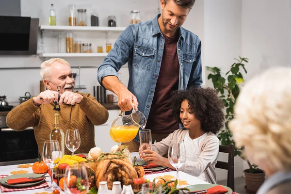 Hombre vertiendo jugo de naranja mientras celebra acción de gracias con la familia multicultural - foto de stock