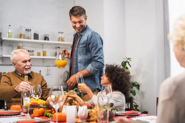 Homem segurando jarro com suco de laranja durante o jantar de ação de graças com família multiétnica — Fotografia de Stock