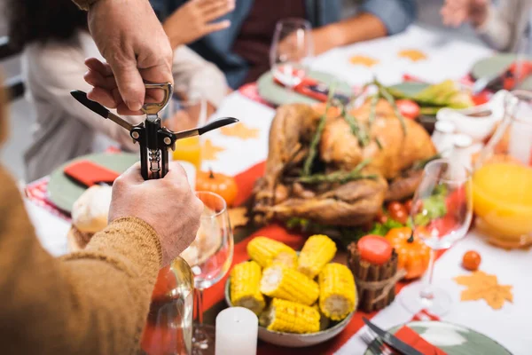 Vue partielle de l'homme âgé ouvrant la bouteille de vin blanc avec tire-bouchon pendant le dîner d'action de grâce avec la famille multiethnique — Photo de stock