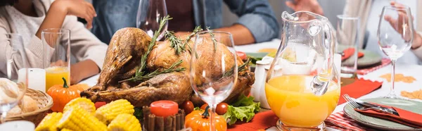Vista ritagliata della famiglia multietnica seduta a tavola con deliziosa cena del Ringraziamento, intestazione del sito web — Foto stock