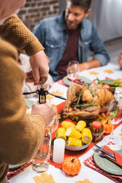 Foco seletivo do homem sênior garrafa de abertura de vinho branco durante a celebração de ação de graças com a família — Fotografia de Stock