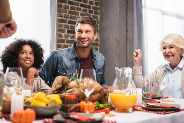 Enfoque selectivo de la mujer mayor mostrando gesto ganador mientras se celebra el día de acción de gracias con la familia multicultural - foto de stock