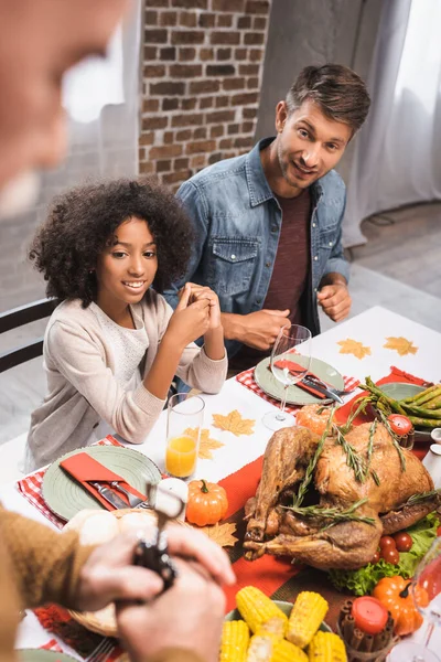 Селективное внимание пожилого человека рядом с мультикультурными отцом и дочерью за столом с праздничным ужином — стоковое фото