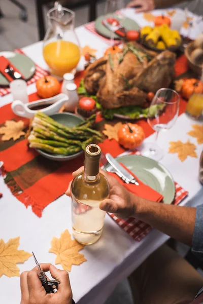 Vista recortada del hombre cerca de la botella de vino blanco en la mesa servida con cena de acción de gracias - foto de stock