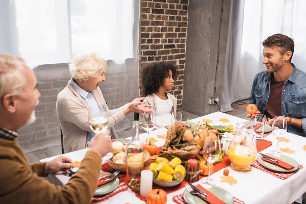 Senior woman gesturing while talking to multicultural family during thanksgiving dinner — Stock Photo