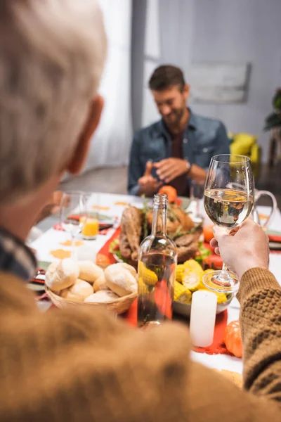 Selective focus of senior man holding glass of white wine during thanksgiving dinner with family — Stock Photo