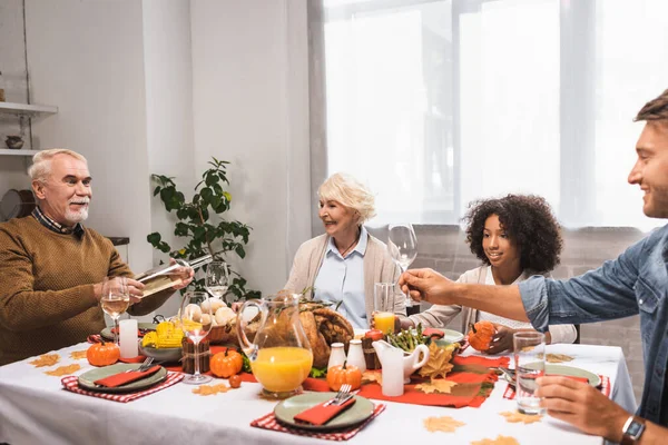 Senior man holding bottle of white wine while celebrating thanksgiving with multicultural family — Stock Photo