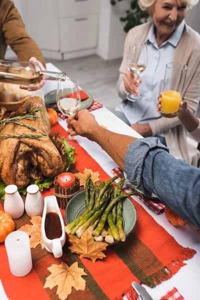 Vista recortada del hombre vertiendo vino blanco mientras celebra la acción de gracias con la familia multicultural - foto de stock