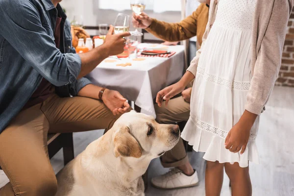 Partial view of african American girl and golden retriever near family clinking wine glasses during thanksgiving dinner — Stock Photo